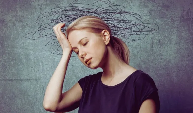 Na obrazie widzimy młodą kobietę z jasnymi włosami, która sprawia wrażenie zmęczonej i przytłoczonej. Jej twarz wyraża smutek lub głęboką refleksję, a dłoń spoczywa na skroni, jakby próbowała złagodzić ból głowy lub opanować natłok myśli. W tle, nad jej głową, znajduje się graficzne przedstawienie chaotycznych, czarnych linii, które symbolizują natłok myśli, stres lub emocjonalne przeciążenie. Obraz silnie oddaje uczucie wewnętrznego niepokoju i dezorientacji, nawiązując do potrzeby znalezienia skutecznych rozwiązań. W kontekście tego wizualnego przekazu warto zastanowić się, jakie są sposoby na negatywne emocje, by odzyskać spokój i równowagę.