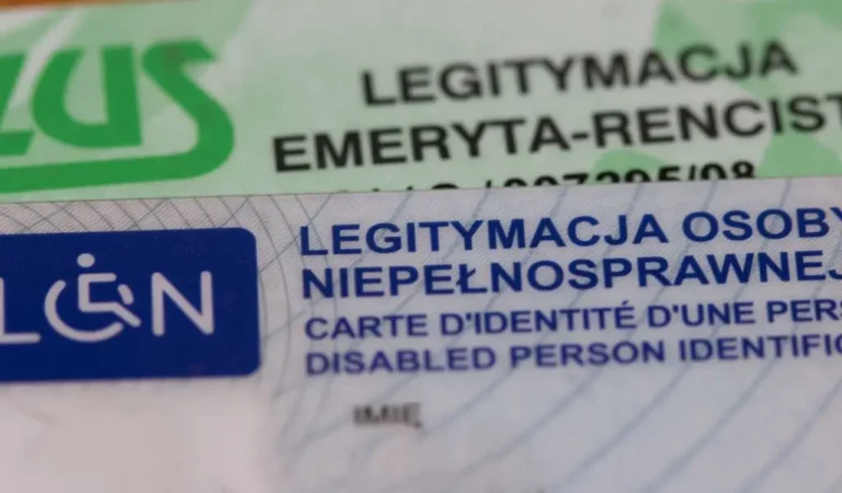 Zdjęcie przedstawia dwie plastikowe karty tożsamości, leżące jedna na drugiej. Na pierwszym planie widoczna jest legitymacja osoby niepełnosprawnej, oznaczona niebieskim symbolem osoby na wózku inwalidzkim. Napisy na karcie są wyraźne, zarówno w języku polskim, jak i francuskim oraz angielskim. W tle częściowo widoczna jest legitymacja emeryta-rencisty, wydana przez ZUS, w odcieniach zieleni. Obie karty są lekko nachylone, co dodaje dynamiki obrazowi. Zdjęcie oddaje powagę i ważność tych dokumentów – stanowią one symbol przynależności do grupy osób wymagających specjalnego wsparcia i uprawnień. Widać w nich zarówno aspekt formalny, jak i pewne emocjonalne znaczenie – towarzyszą one codziennemu życiu ich posiadaczy, niosąc zarówno ulgę w trudach, jak i przypomnienie o istniejących barierach.