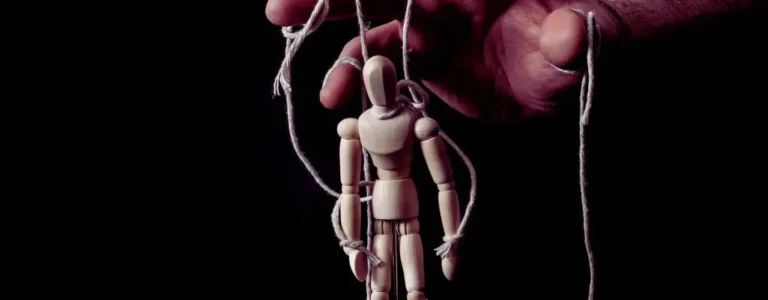 Na obrazku widać drewnianą figurkę ludzika zawieszoną na sznurkach, trzymanych przez dużą, ludzką dłoń. Całość przypomina marionetkę kontrolowaną przez niewidzialnego lalkarza. Ciemne tło i kontrastowe oświetlenie potęgują uczucie zniewolenia i braku kontroli. Obraz symbolicznie przedstawia sytuację, w której człowiek staje się narzędziem w rękach manipulanta. Doskonale ilustruje temat: Jak bronić się przed manipulacją – ukazując, jak łatwo można zostać wciągniętym w cudzą grę, jeśli nie jest się świadomym własnych granic i emocji.