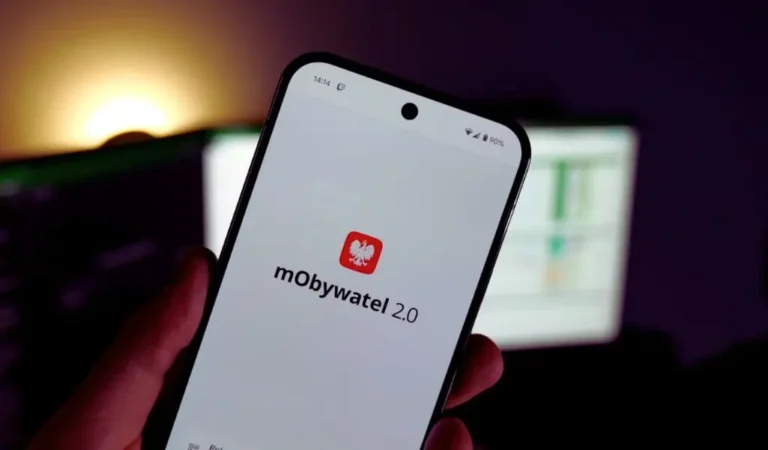Na zdjęciu widać dłoń trzymającą smartfon, na którego ekranie wyświetla się logo aplikacji mObywatel 2.0 – biały ekran z czerwonym symbolem orła i napisem. Obrazek oddaje poczucie nowoczesności, wygody i prostoty w korzystaniu z cyfrowych dokumentów. Jasne światło w tle tworzy atmosferę lekkości i swobody, sugerując, że cyfrowe rozwiązania ułatwiają codzienne życie. To wizualna metafora tego, jak łatwe i bezpieczne może być zarządzanie dokumentami online, na przykład jak dodać e-legitymację osoby niepełnosprawnej w mObywatel.